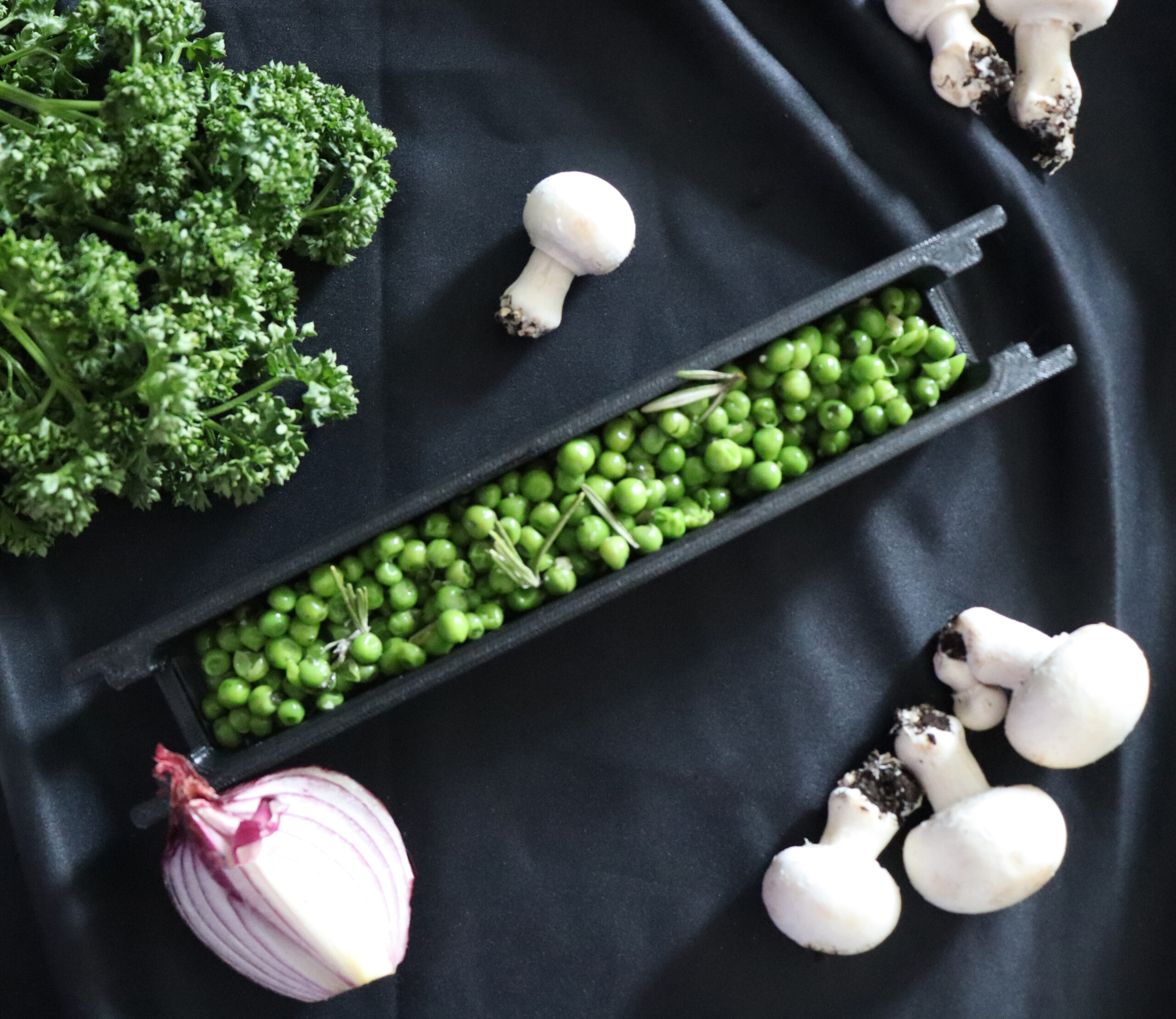 Photo culinaire : petit pois dans un petit compartiment avec des aliments autour pour décorer (persil, champignons, oignon)